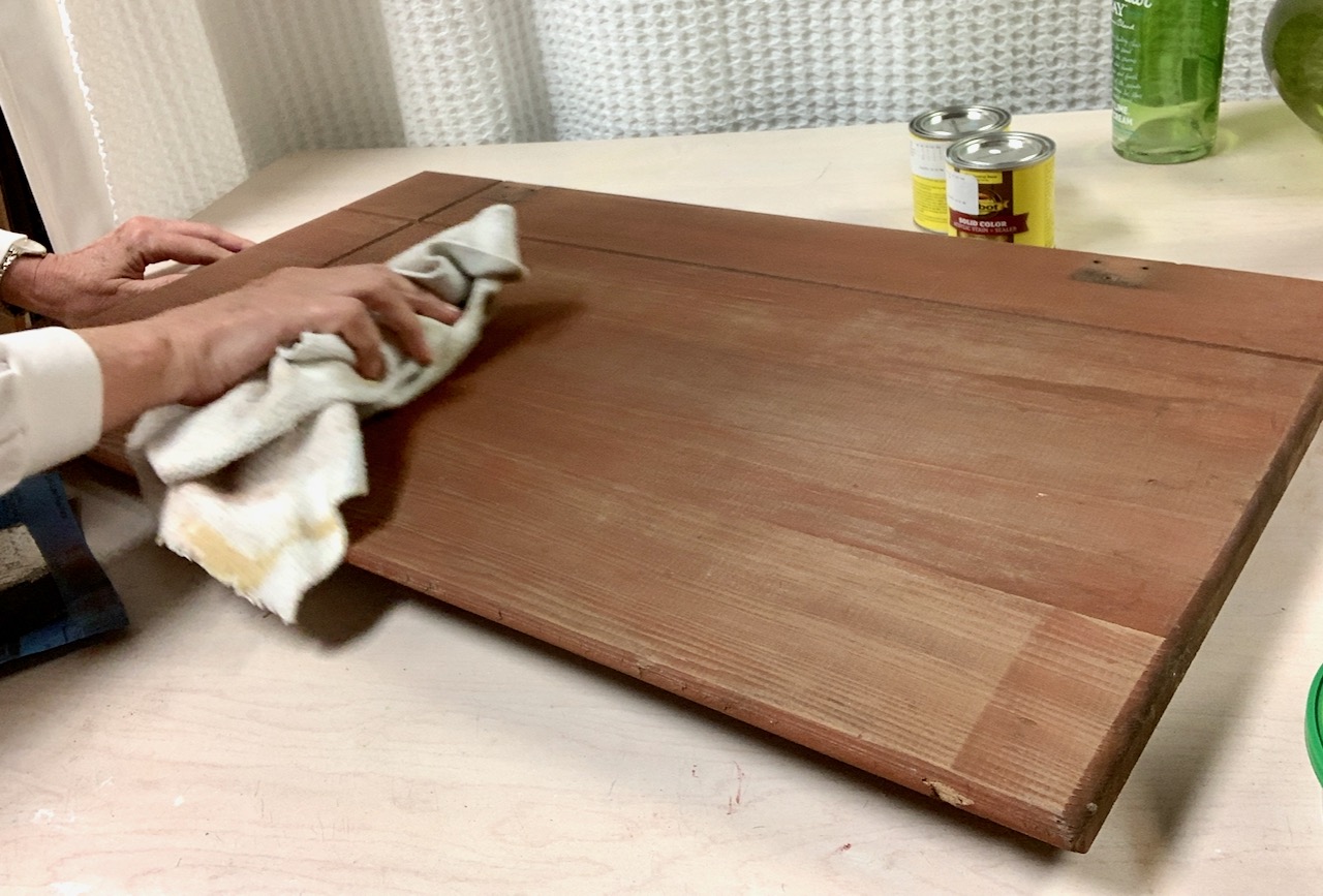 hand holding cloth wiping off the dust on.a newly sanded cabinet door