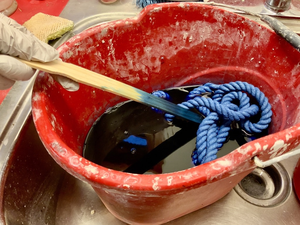 The rope in the bucket of dye with a hand stirring the rope in the dye