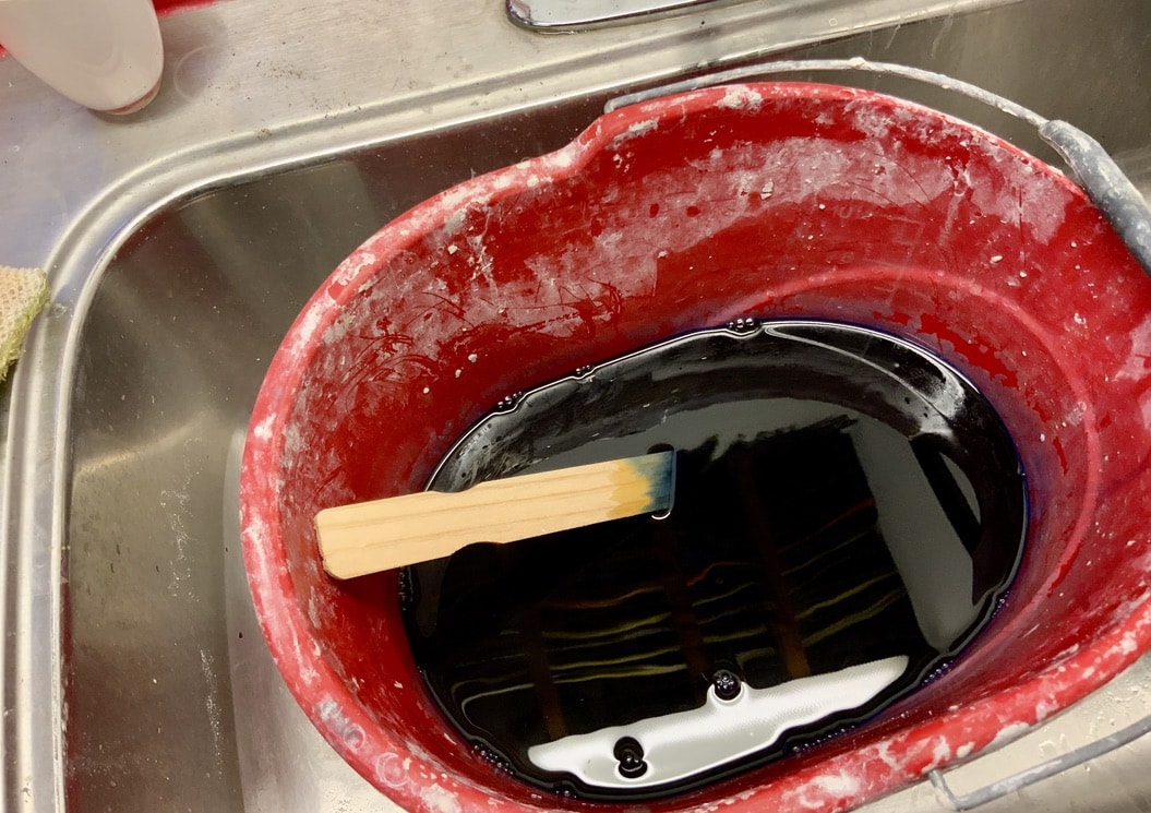 Bucket with water and dissolved dye with a paint stick for stirring