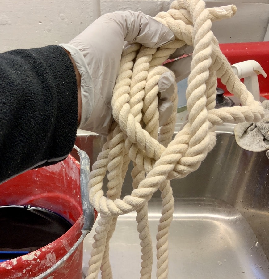 A gloved hand holding the length of natural rope ready to be pre-soaked