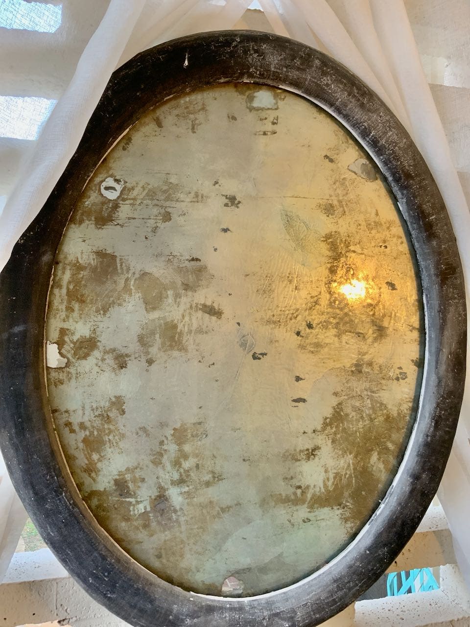 A large oval mirror with an aging technique that mottled the reflective glass