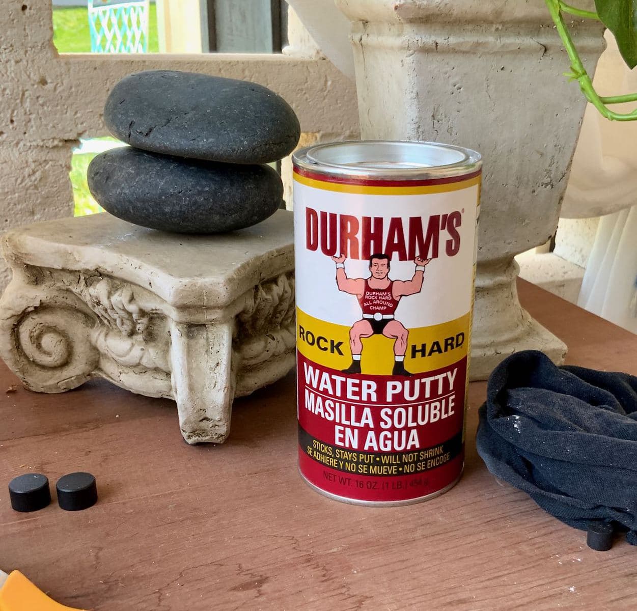 A can of Duham's Hard Rock Water Putty sitting on our patio cabinet with a rag next to it and some decorative pots behind it.