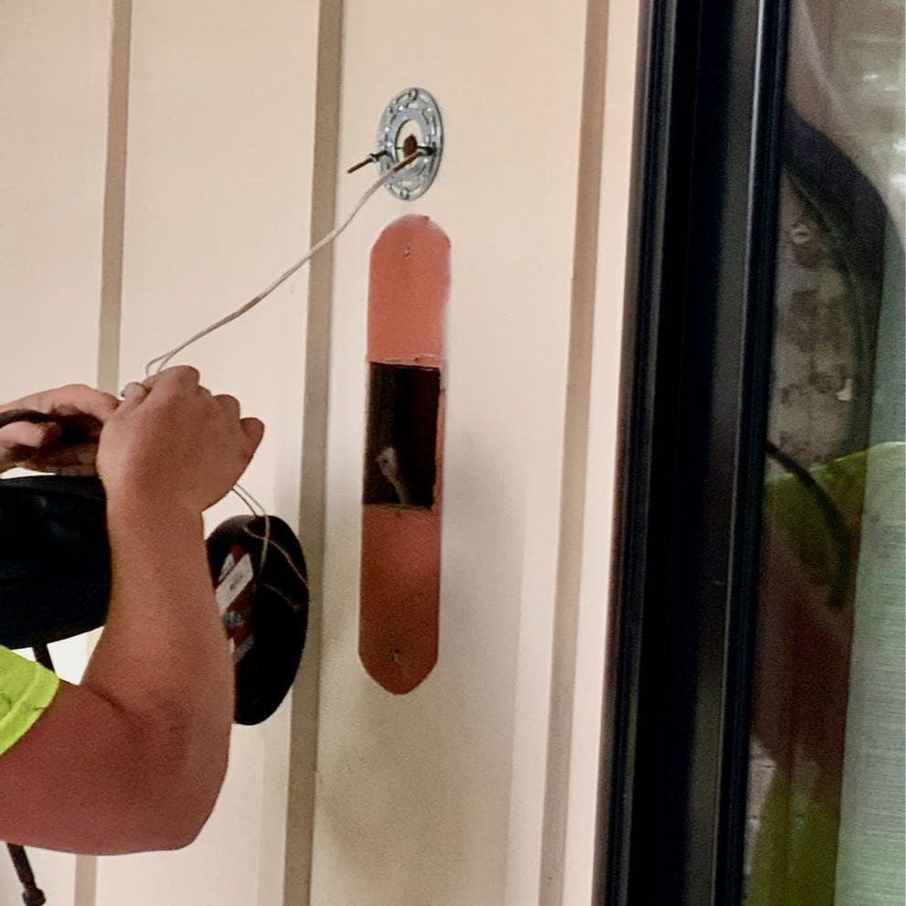 Man's arms wiring a new light fixture in place above a large hole in the exterior wall