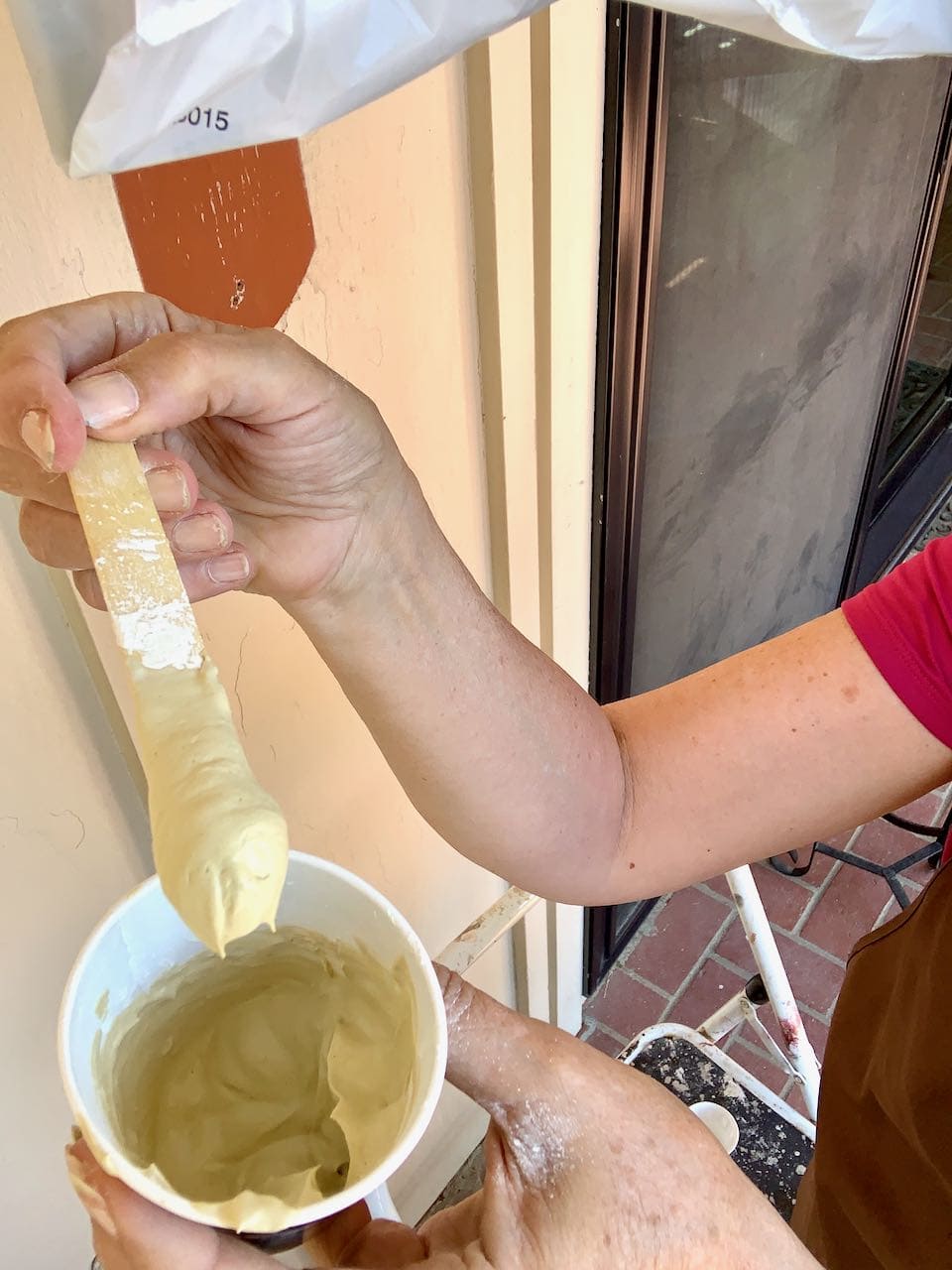a paper cup held in one hand with the other hand and arm showing a craft stick with the thick mixed putty clinging to it 