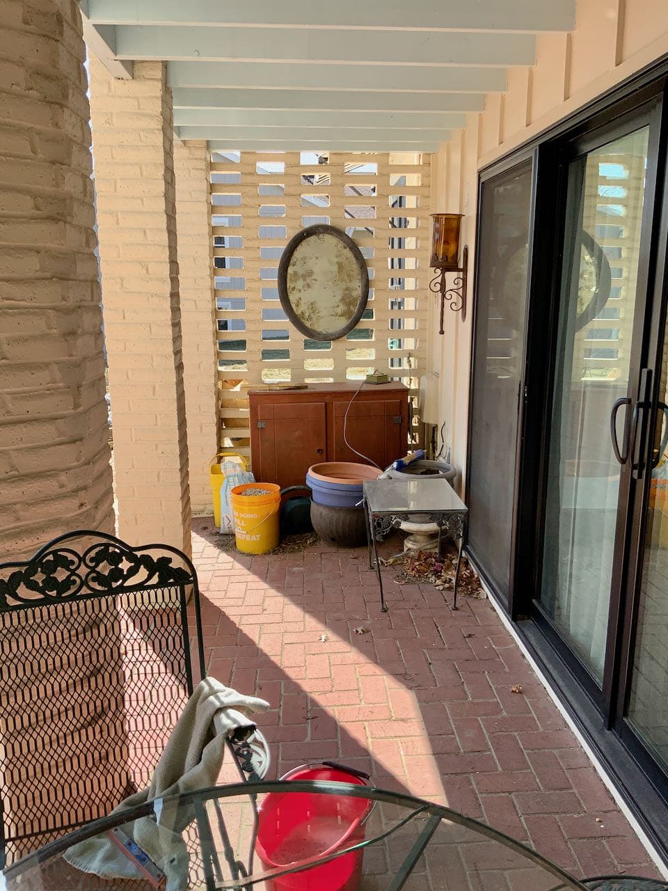 long view of corner of patio with red brick floor and a jumble of "stuff" accumulated 