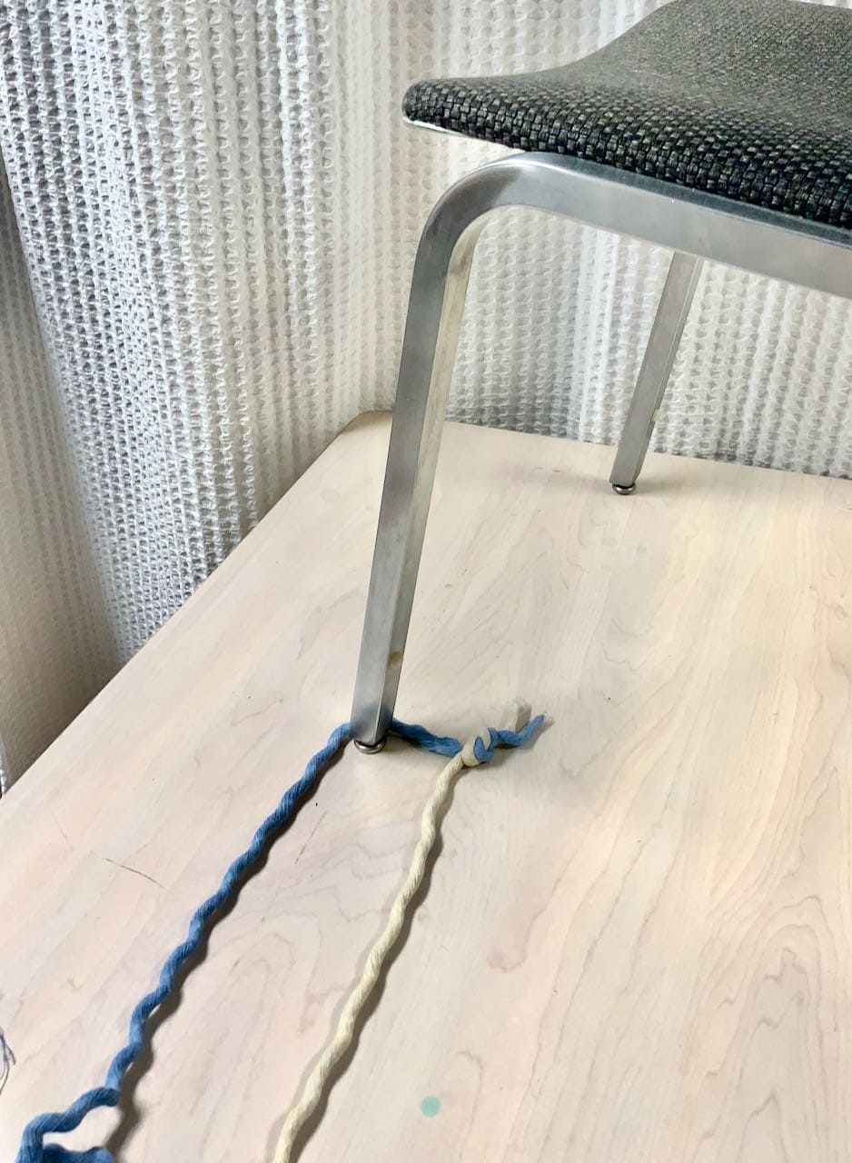 The two strands tied together straddling the leg of a chair