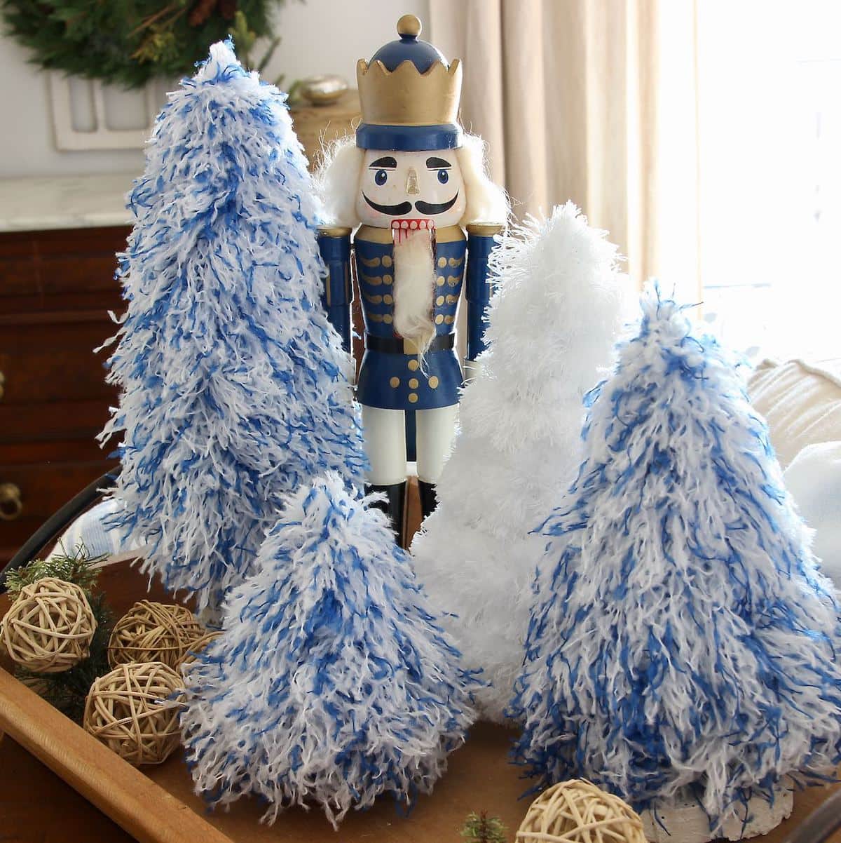 Blue Wooden Soldier surrounded by blue and white fluffy Christmas trees on a wood tray