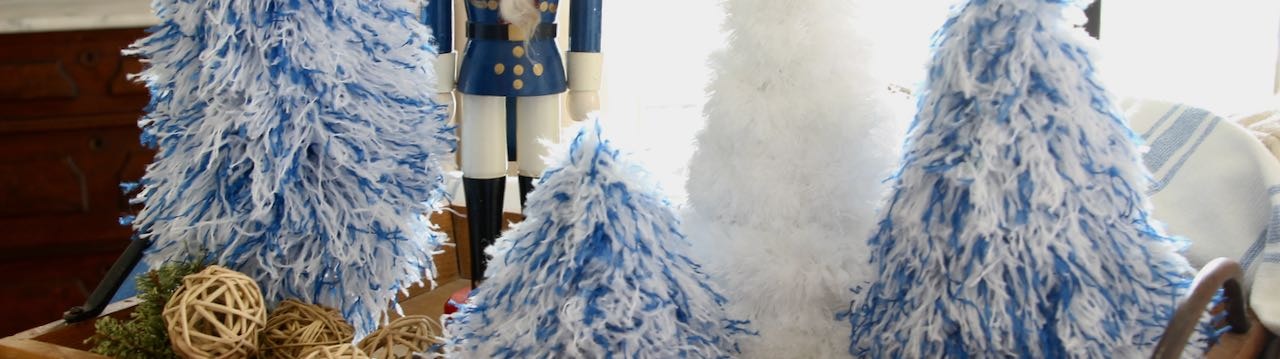 Short wide partial view of three fluffy blue and white Christmas trees with an additional white tree and part of a blue and white wooden soldier 