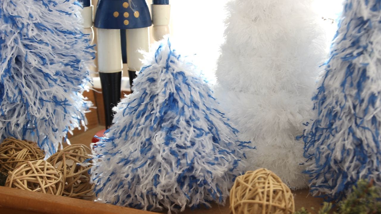 Close up view of short blue & white fluffy Christmas tree with all white tree and the legs of a wooden soldier showing behind