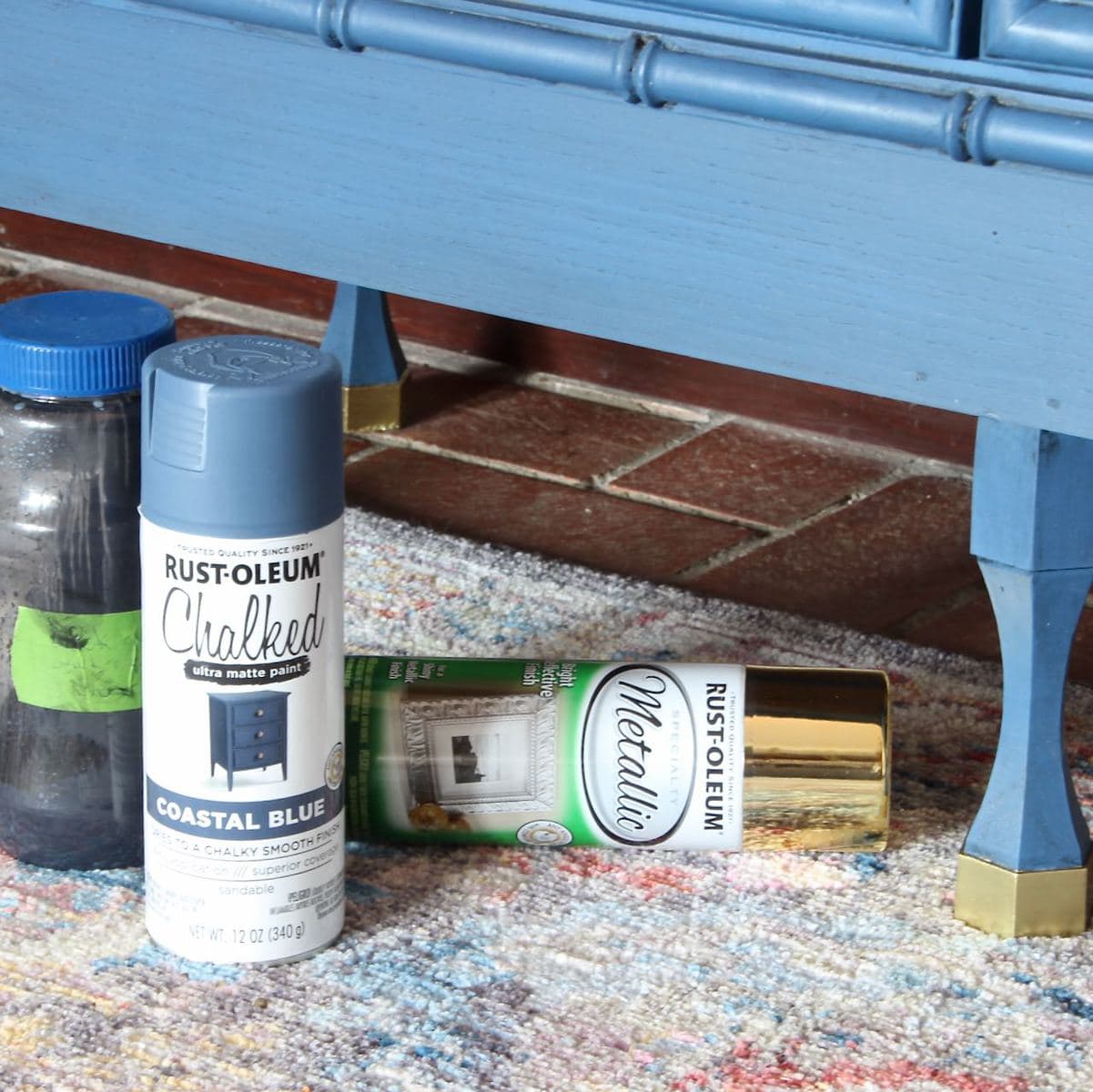 Two cans of Spray Paint and one jar of homemade glaze on the area rug by the chest