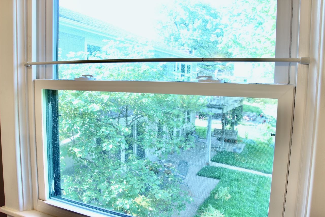 The view out the bathroom window showing the neighbors patio and deck and a tension rod suspended where the privacy is wanted below and the view and light above