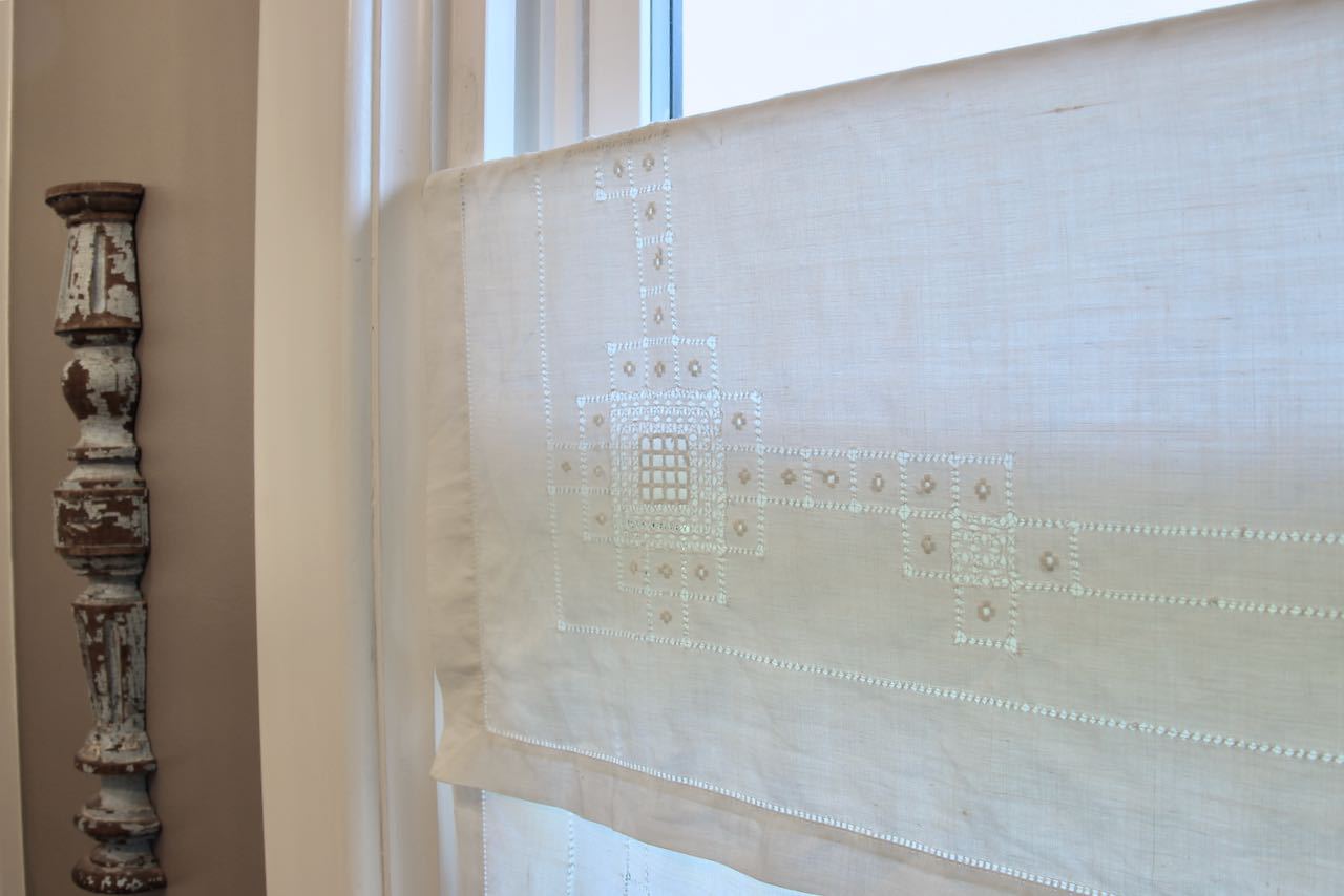 Closeup of detailing on a vintage table cloth hanging over a tension rod in a bathroom window