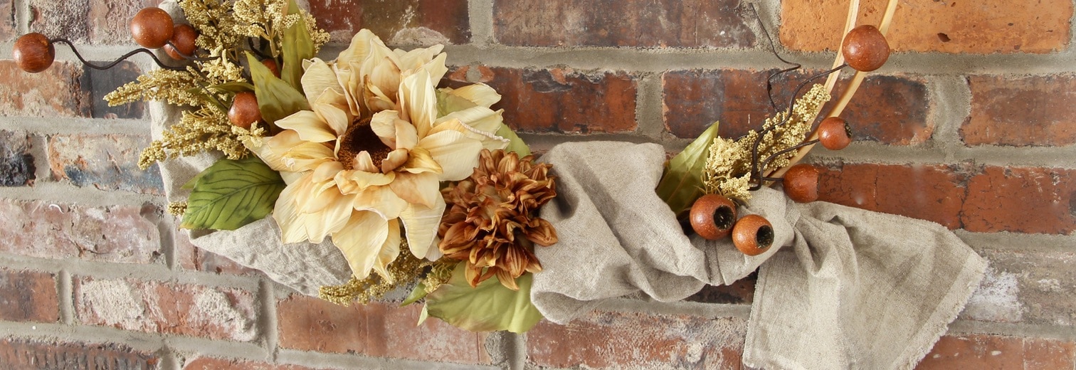 Closeup of Sunflower and linen table runner with other Fall filler flowers on a double hoop wreath against a brick wall