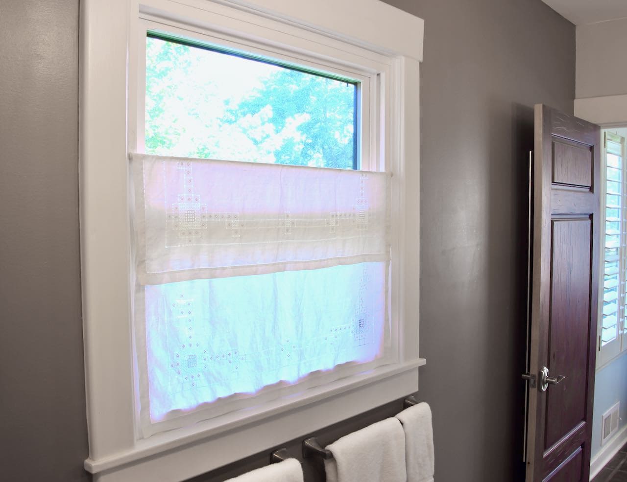 angle view of bathroom window with square vintage table cloth with beautiful handwork detailing stitched in place over a tension rod