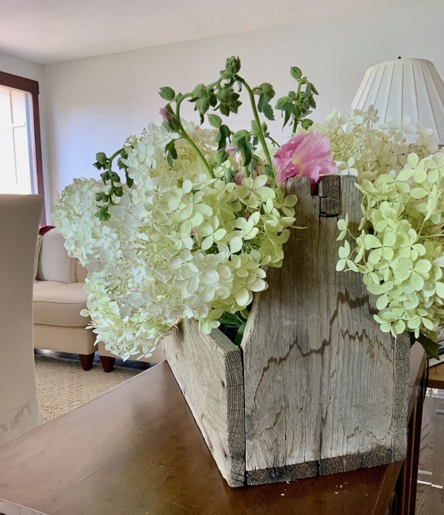 view of the end of the vintage wood tool kit filled with hydrangeas and storm ravaged Hollyhocks