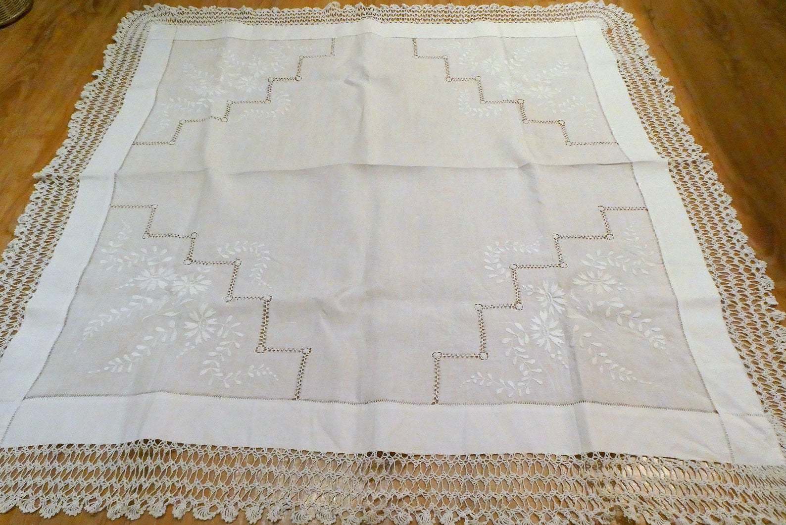 a vintage tablecloth spread out showing it's inticate geometric cutwork detailing