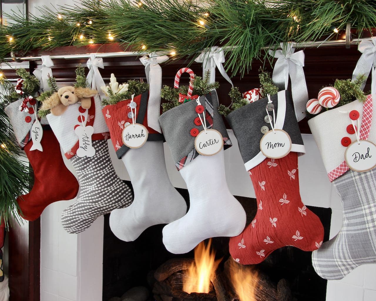 Angle view of Preppy Christmas Stockings tied up with silver bows and with white birch tree slice name tags hanging from the top button on each stocking cuff