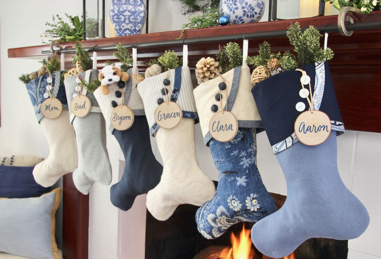 Angle view of The Blues Christmas stockings with birch tree slice ornaments hanging from their cuff buttons all hanging from a Dark wood mantel