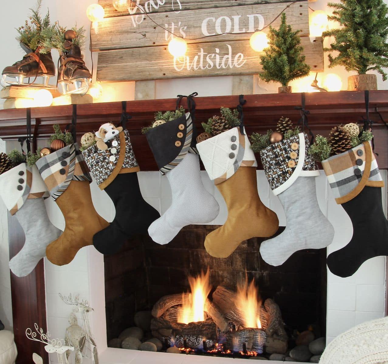 7 Casual Cozy Christmas Stockings below a "Baby, It's Cold Outside" sign made of reclaimed wood with globe lights and vintage ice skates