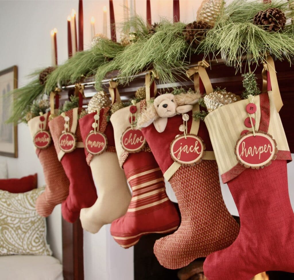 angle view on red and gold christmas stockings with red ree slice name tags beneath a layer of long needle pine and gold and burgundy tapers