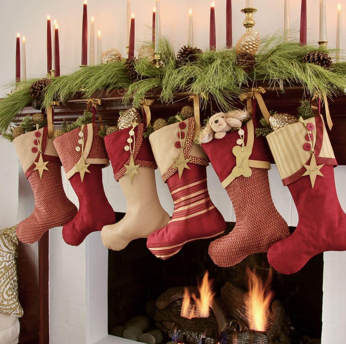 Red and Gold Christmas Stockings with gold star name tags hanging below long need pine and 24 gold and burgundy taper candles