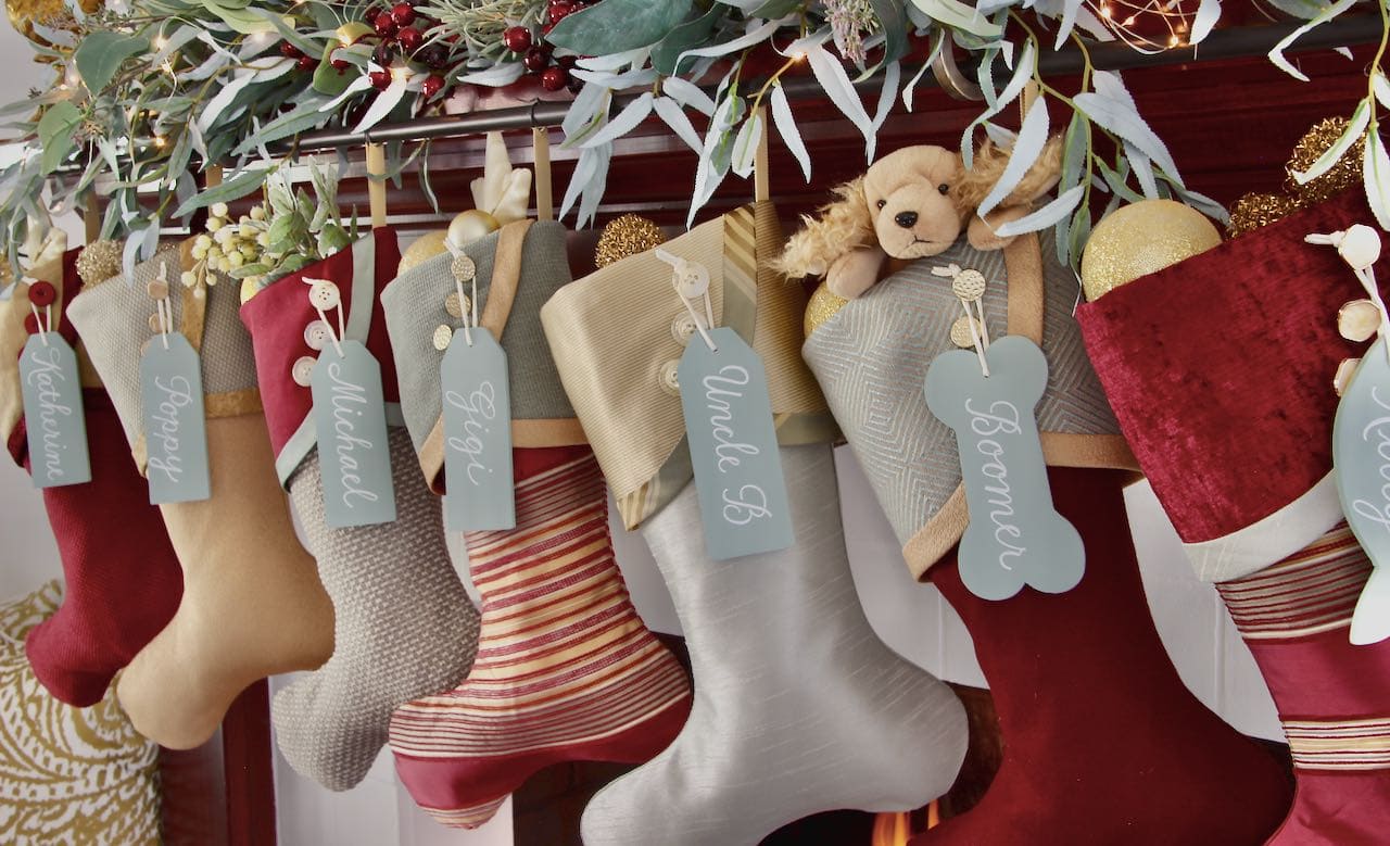 Row of 7 Burgundy and Teak Christmas stockings with large seafoam name tags hanging on their cuff buttons