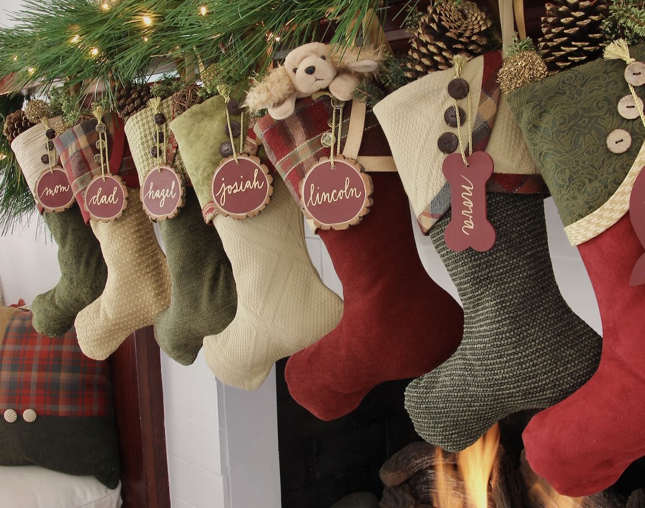 Row of 7 Deep Traditions Christmas Stockings all with burgundy tree slice name tags hanging from the top button on their cuffs