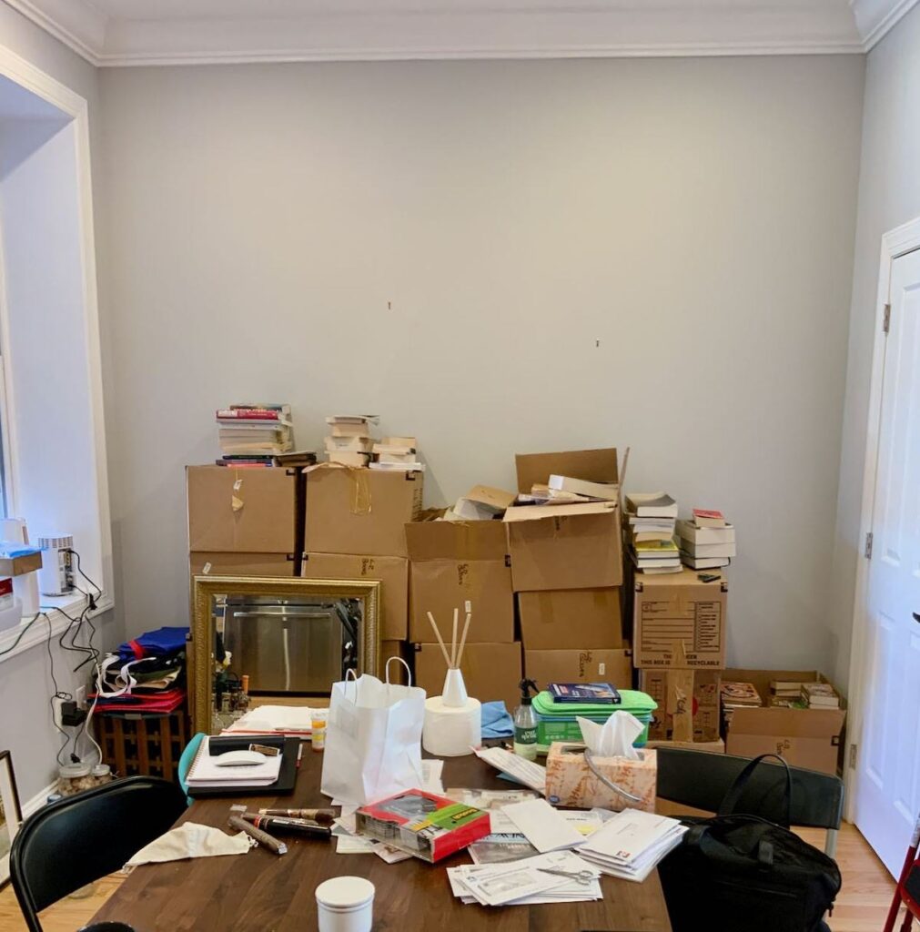 Before image of the boring, flat grey dining room wall filled with boxes and books