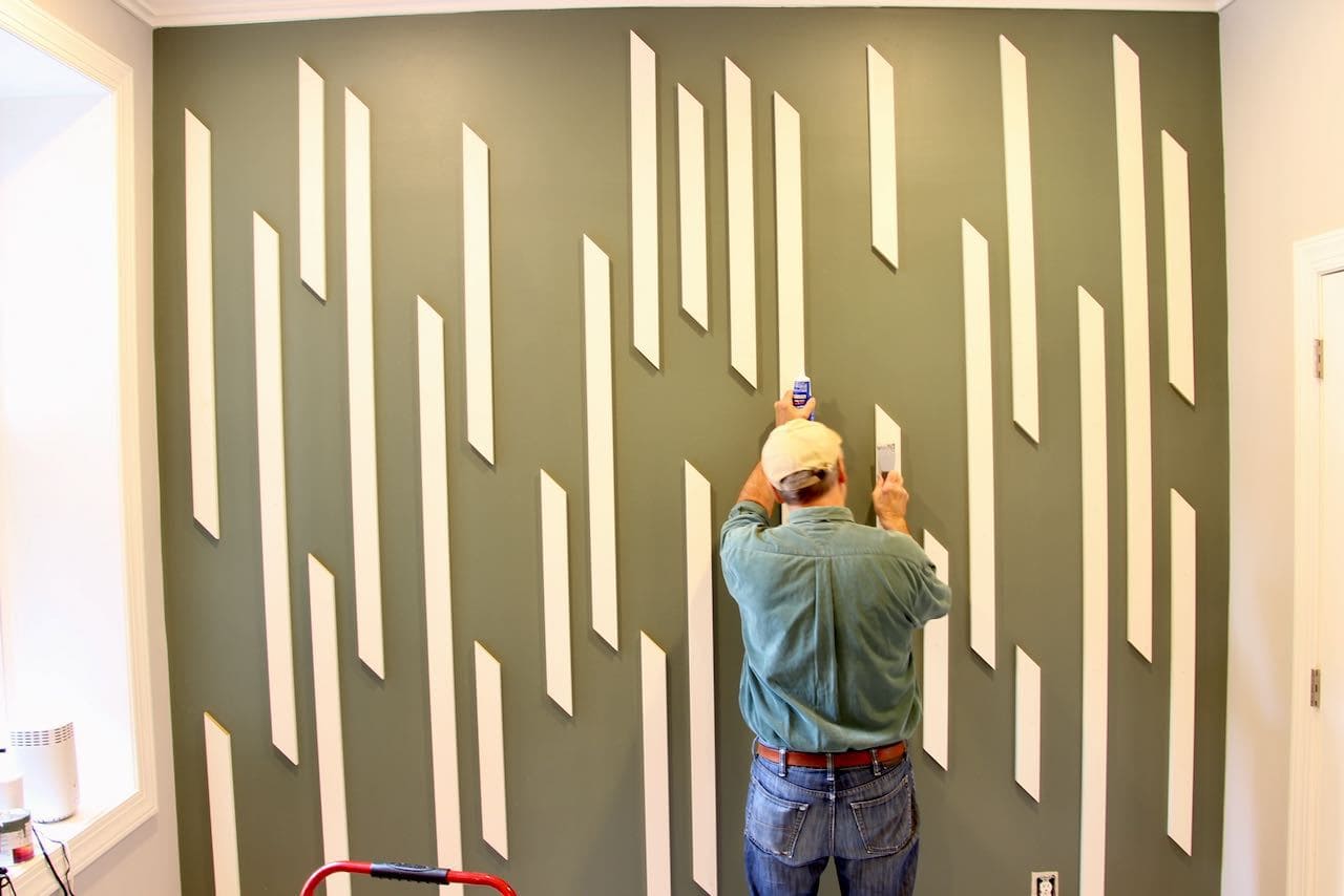 Primed wood slats on wall with the back of a man shown filling nail holes with puddy