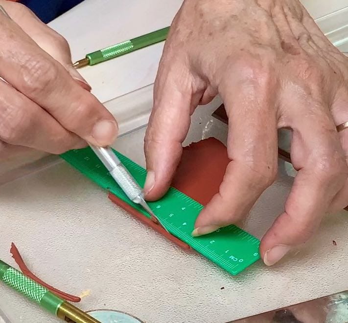 Hands using a straight edge to cut thin slices of polymer clay