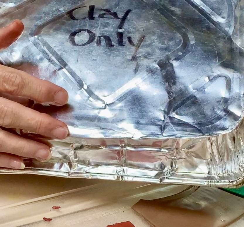 A second foil baking dish is inverted over the bottom to asct as a lid with marker on top "Clay Only"