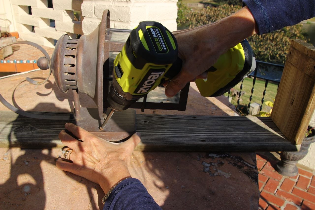 Hand holding a Drill attaching a vintage lantern to the reclaimed wood post