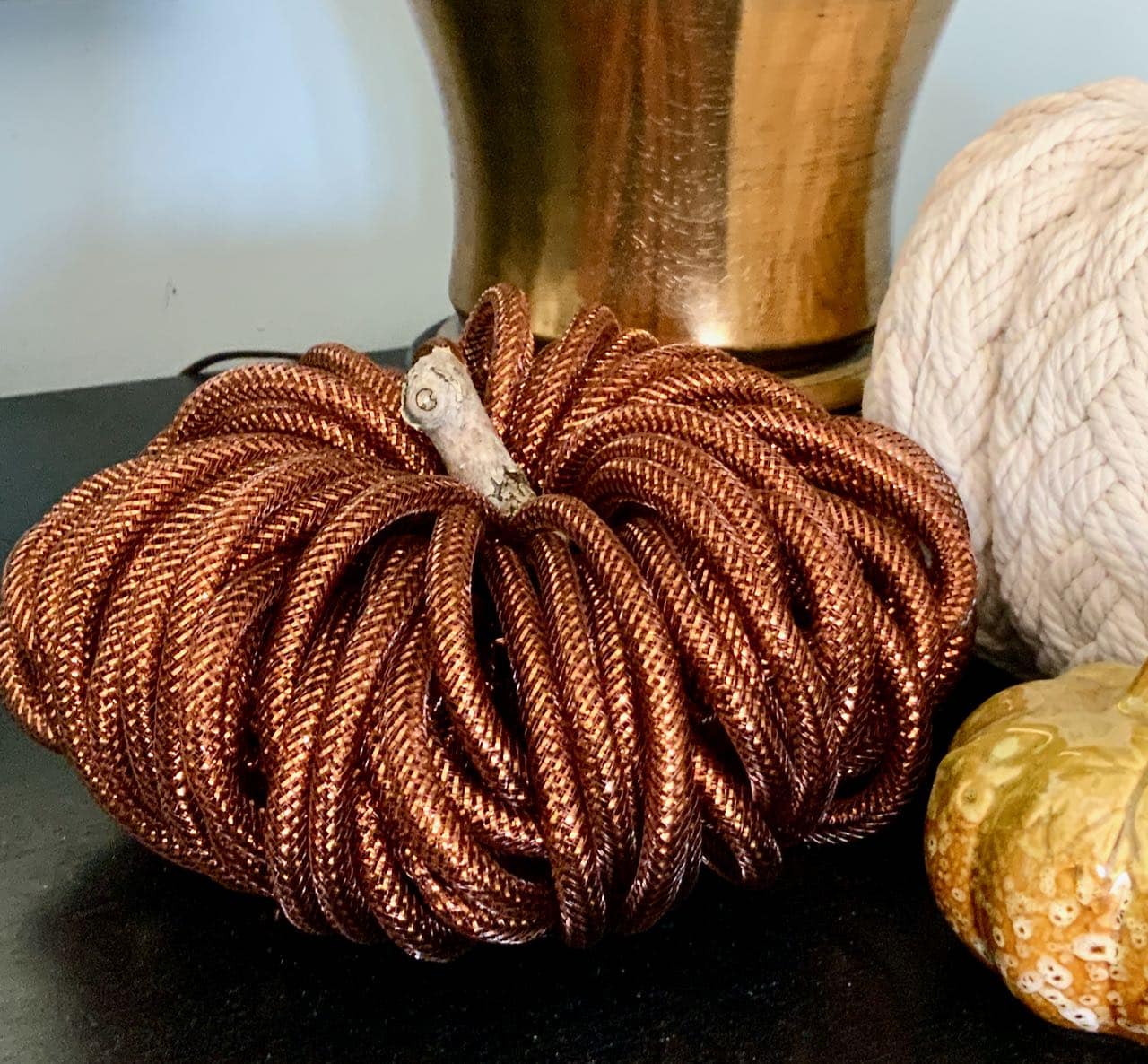 closer view of the five finished metal mini pumpkins arranged on a stack of black wood risers on a wood table with a washed linen table runner and scattered Fall leaves