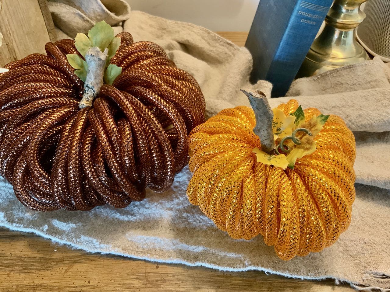 close-up view of the tops of the two mesh pumpkins with the stick tems showing with artificial leaves added by the stem