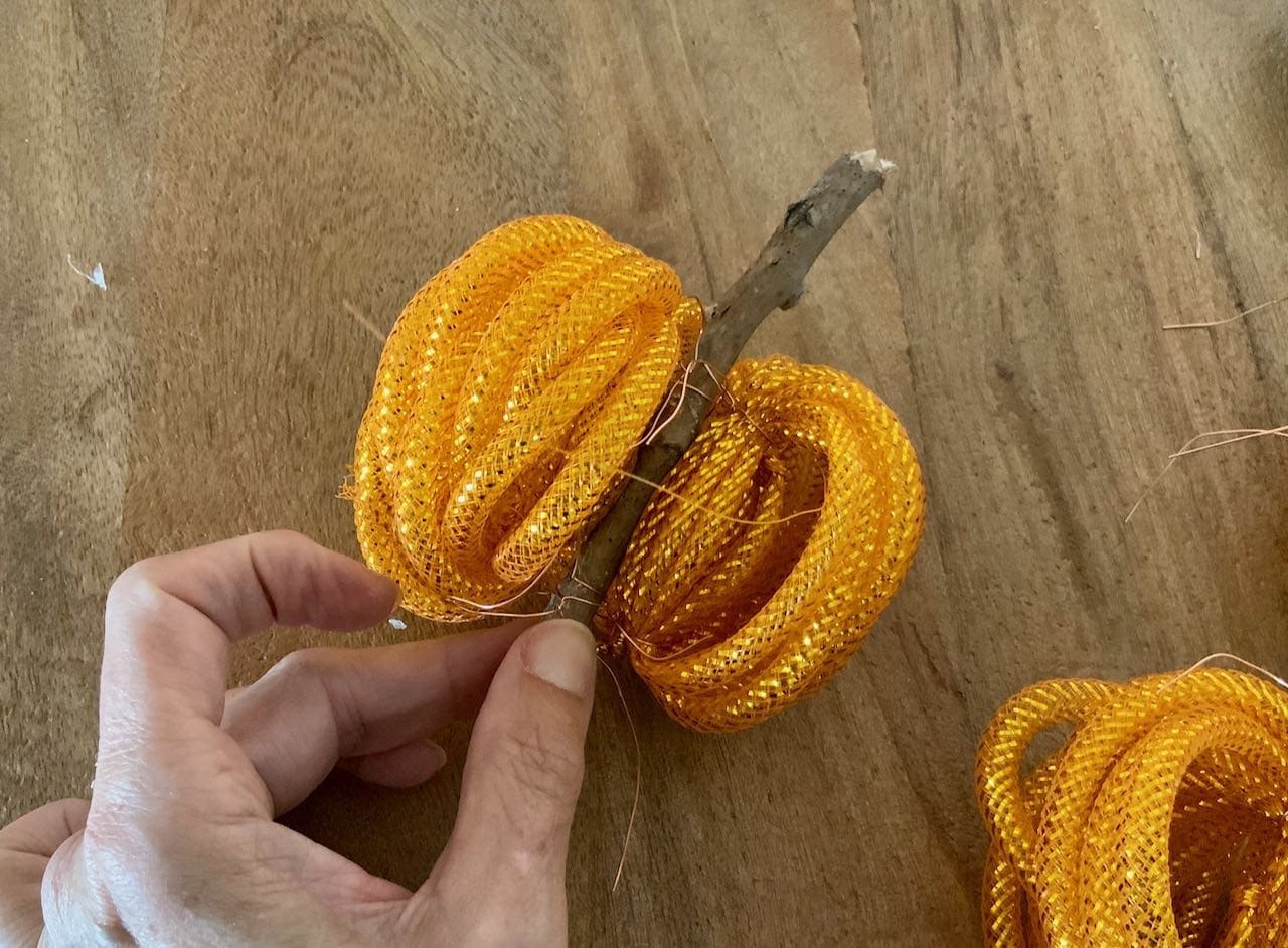 a hand holding a stick stem with two bundles of the golden orange mesh wired around the stem at the top and bottom of the bundles