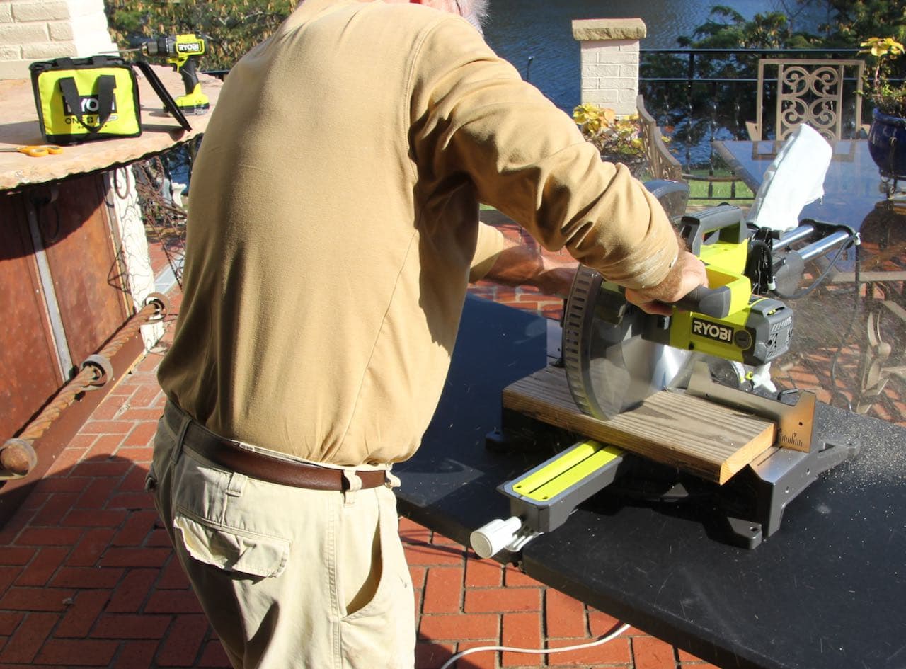partial view of a man using a ryobi sliding compound miter saw to cut distressed wood planks