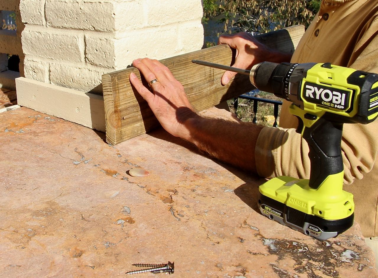 hands holding one plank against a brick wall to begin forming a post