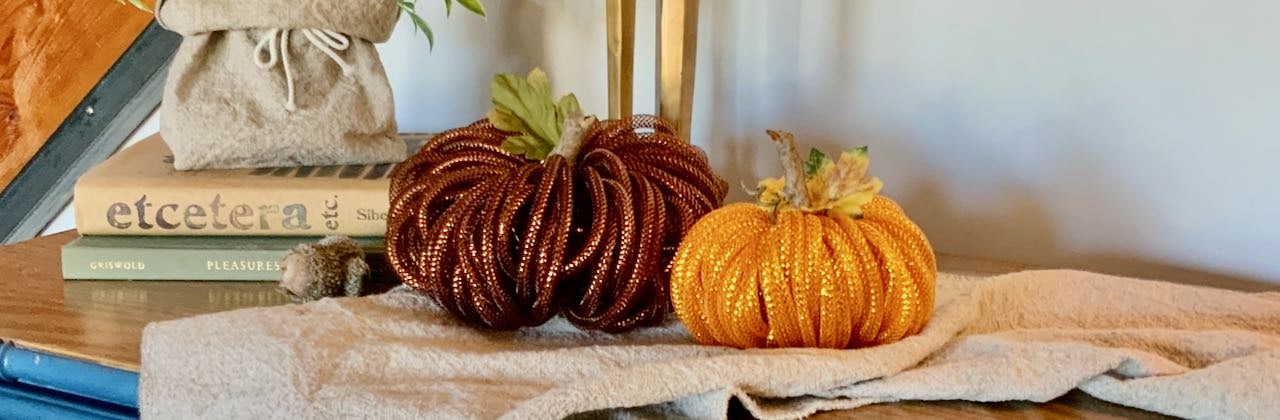 Closeup of two mesh tubing pumpkins with faux leaves  on a washed linen table runner