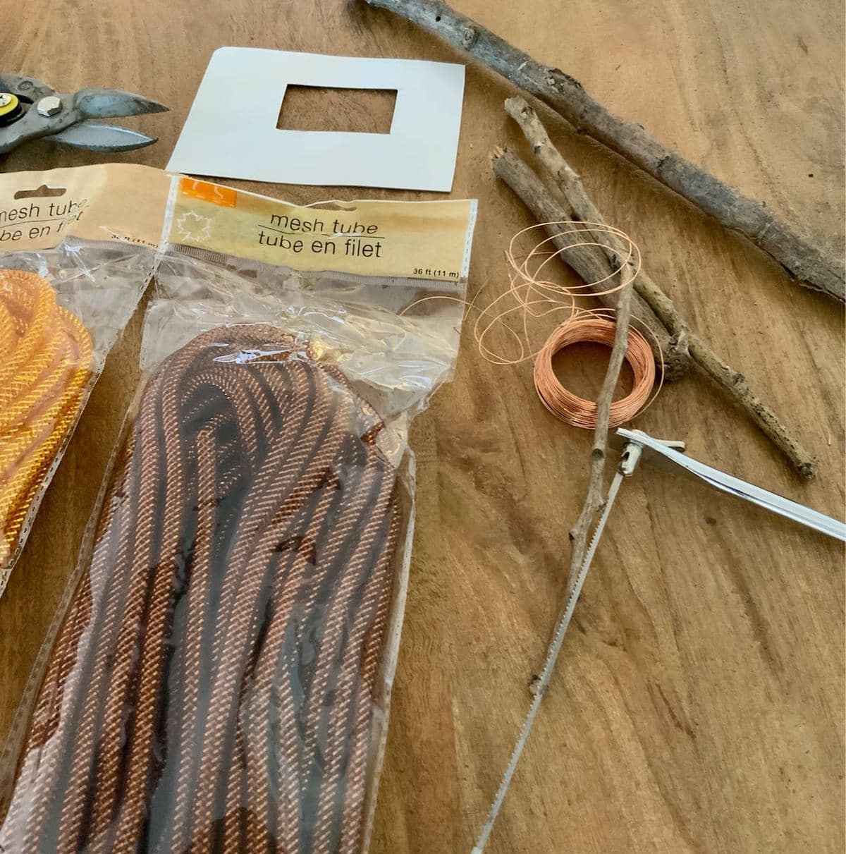 Supplies to make mesh tubing pumpkins are laid out on a wood table