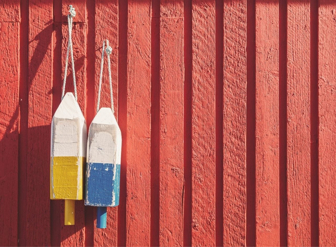old faded painted exterior wall of a boat house with two wooden buoys hanging off centerg