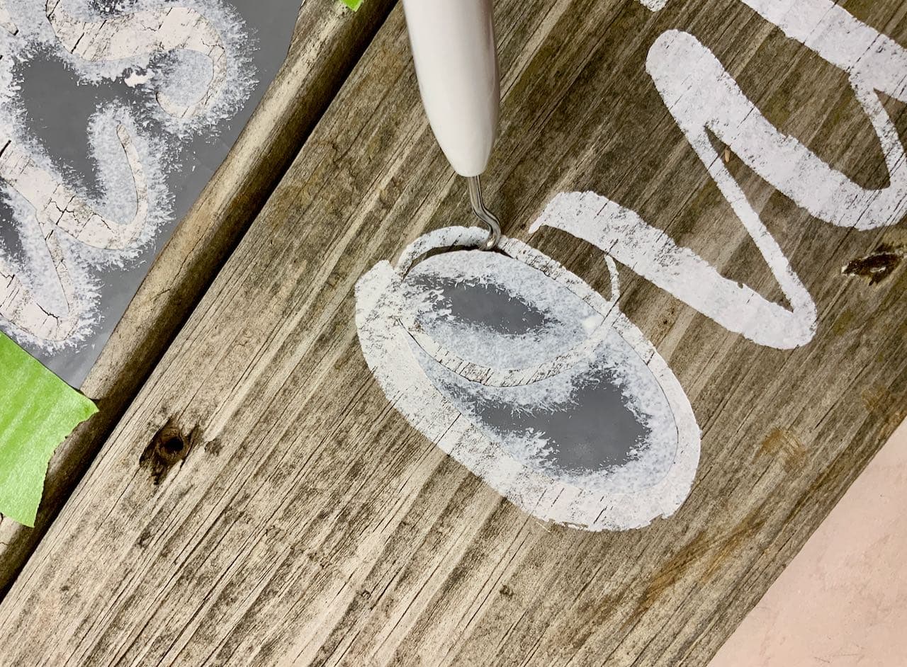 closeup of the tip of a Cricut weeding tool pulling off the stencil