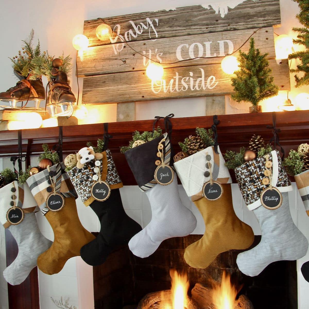 Full view of wood mantel with 7 Cozy Copper Christmas stockings hanging below and ice skates, snowball lights and a large reclaimed wood sign that says "Baby, it's cold outside