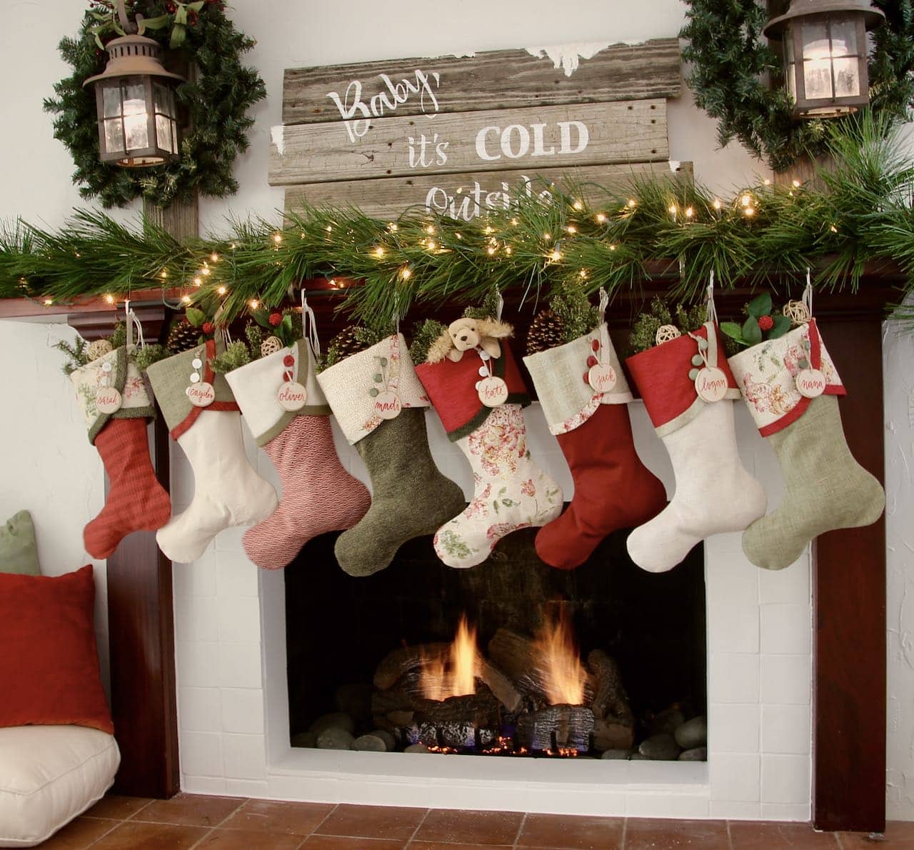 Full length front view of calssic cottage mantel featuring two lanterns with wreaths flanking a large reclaimed wood sig that reads "Baby, it's cold outside"