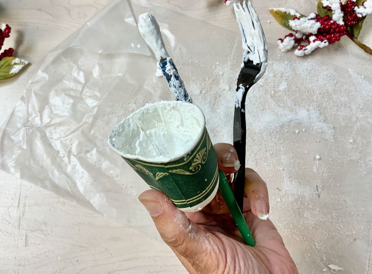hand holding a paper dixie cup with a paintbrush and a plastic fork used for mixing