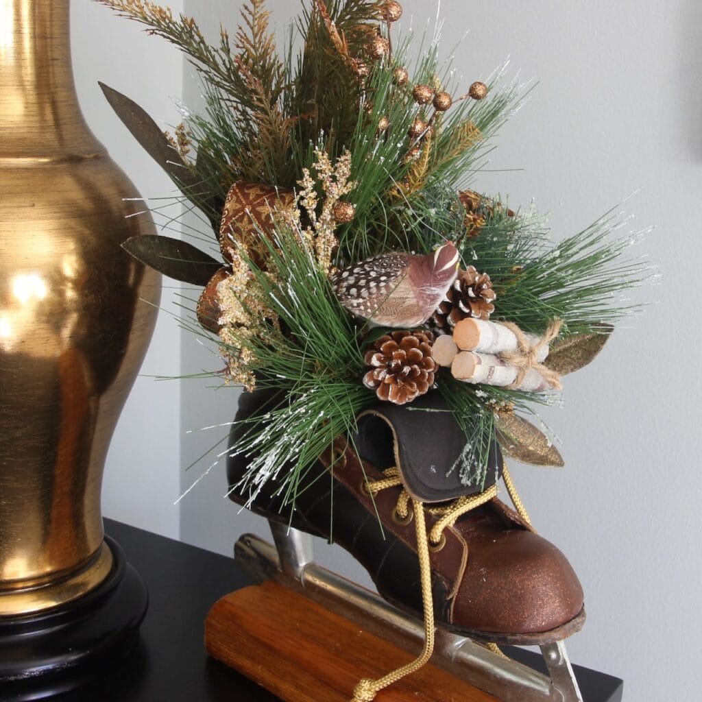 Cloeup of vintage ice skate on a stained wood block with fir branches, a bird, little bundle of birch logs arranged in the open boot of the skate
