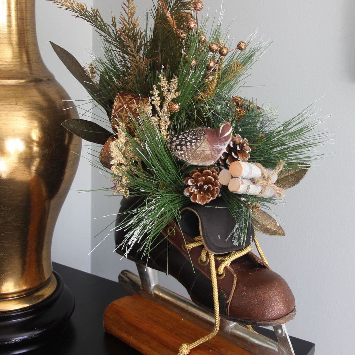 Cloeup of vintage ice skate on a stained wood block with fir branches, a bird, little bundle of birch logs arranged in the open boot of the skate