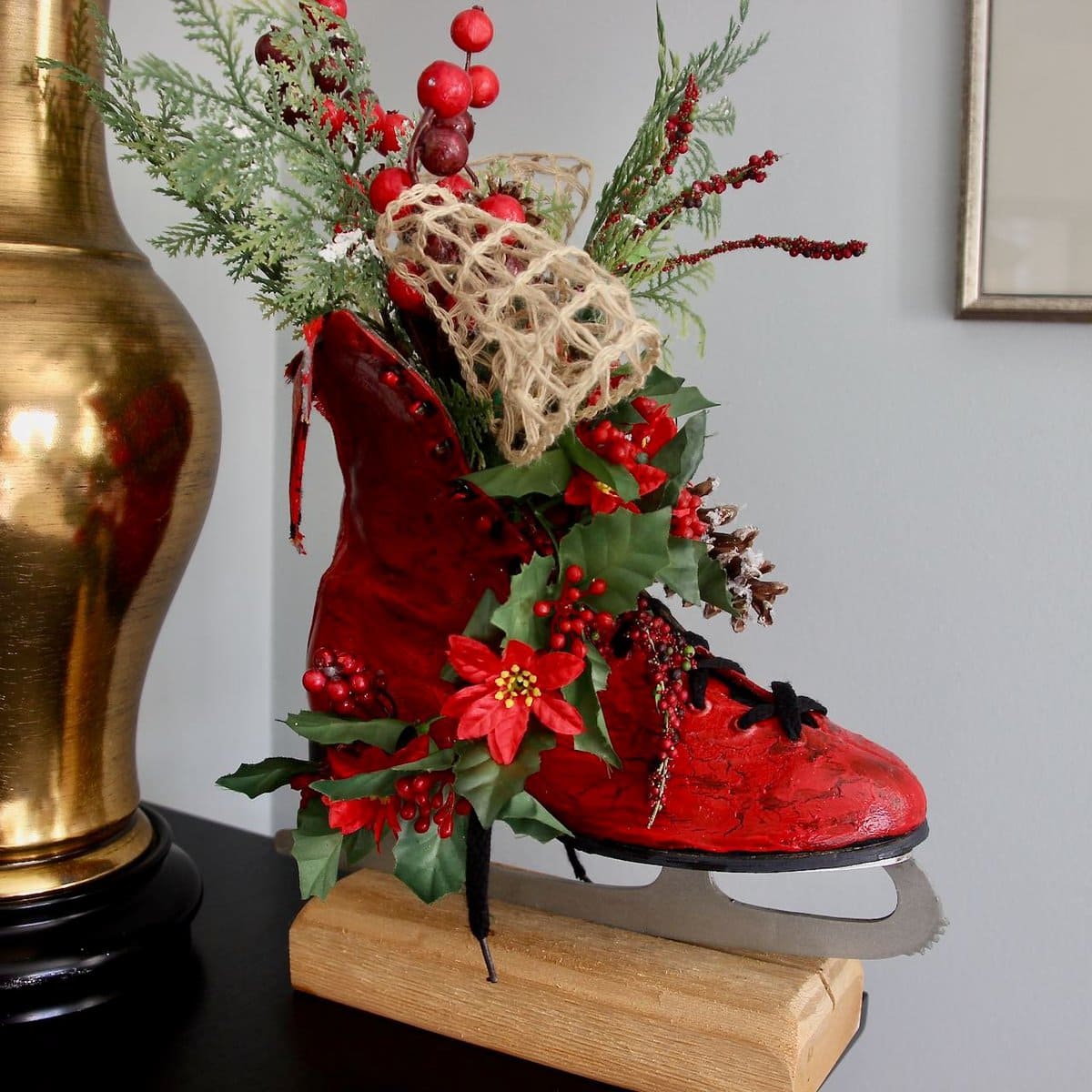 Vintage ice skate painted red and arranged with Christmas greens and poinsettia and burlap ribbon flowing from the top of the skate