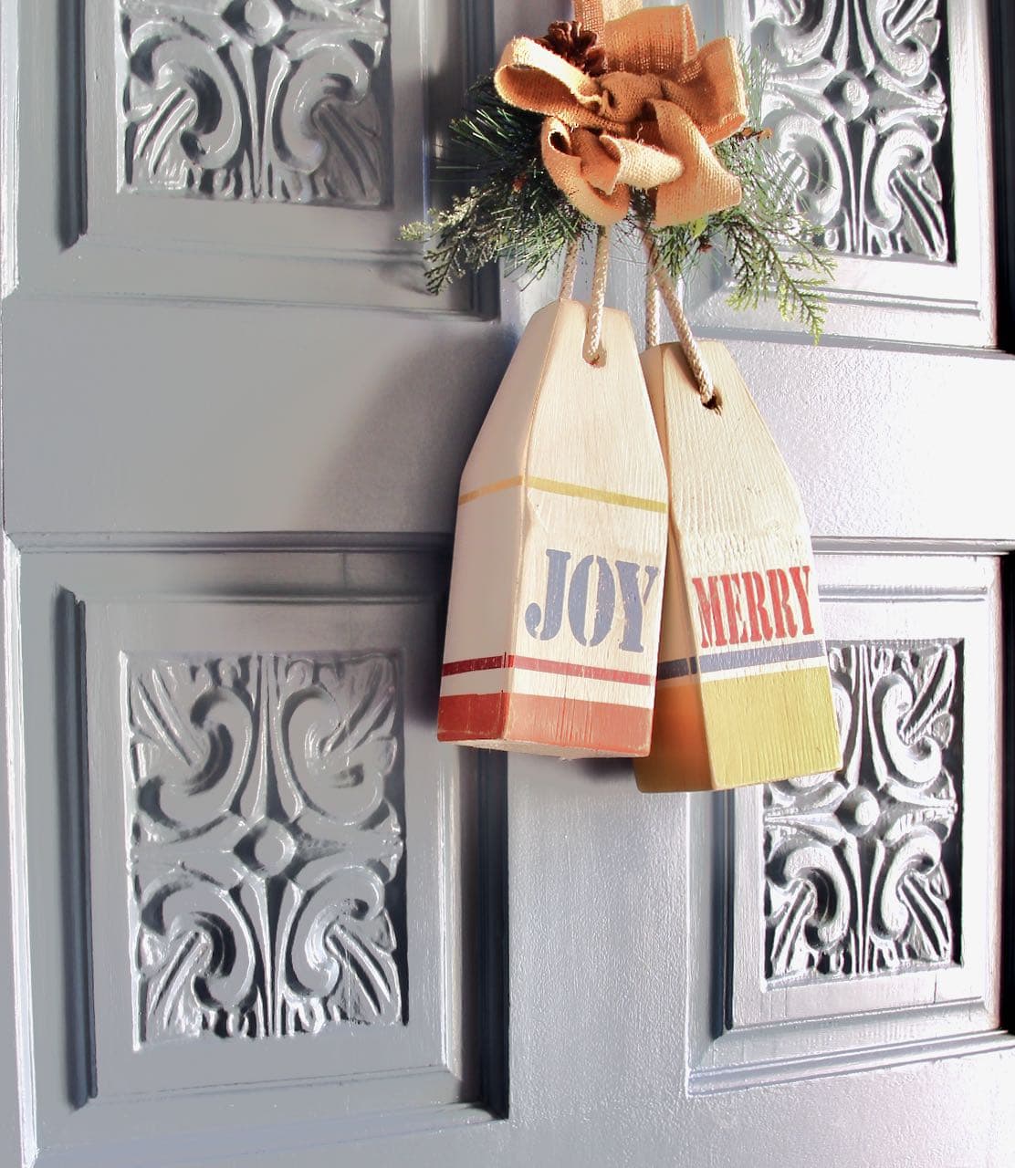 "Merry" and "Joy" wood buoys hanging from a burlap bow with greens on a painted carved wood front door