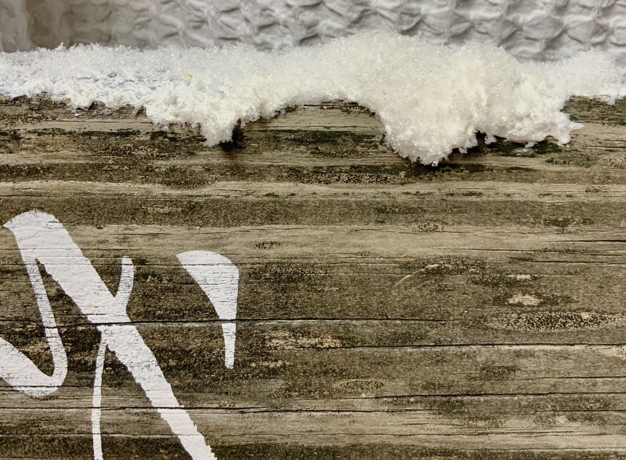 super closeup of the detail of paint and faux snow as it appears to drift on top of the wood sign