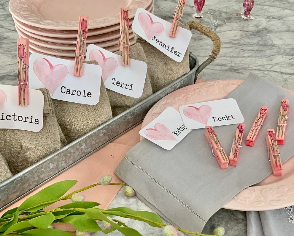 Pink plates, linen naokins, spring bud and a tray of linen party favor bags are all ready to a Galentines party 